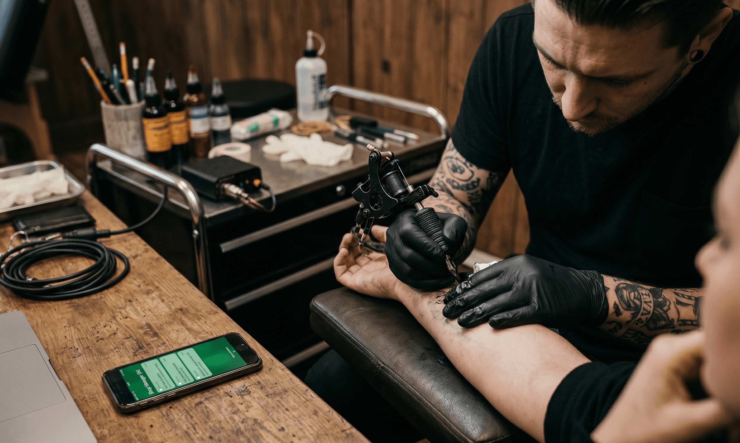 Tattoo artist at a desk surrounded by a laptop and phone, writing out quotes, not tattooing